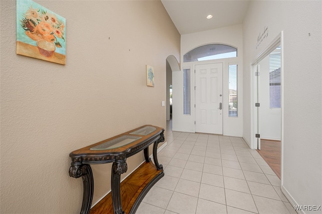 foyer entrance featuring light tile patterned floors, baseboards, and arched walkways