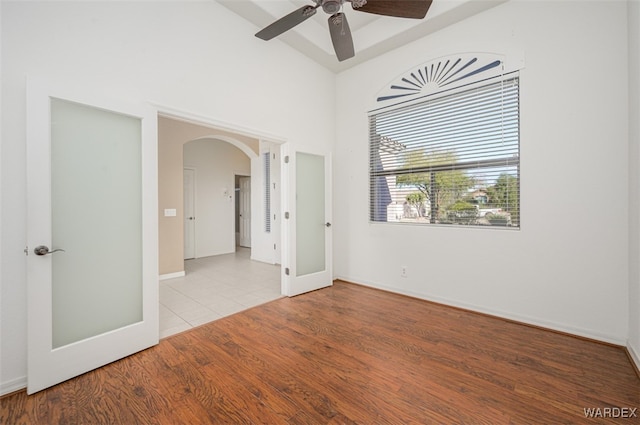 spare room featuring arched walkways, a high ceiling, wood finished floors, a ceiling fan, and baseboards