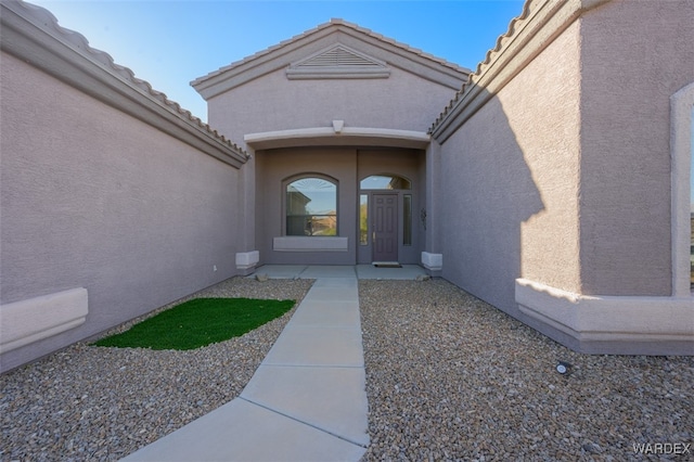 view of exterior entry featuring a tiled roof and stucco siding