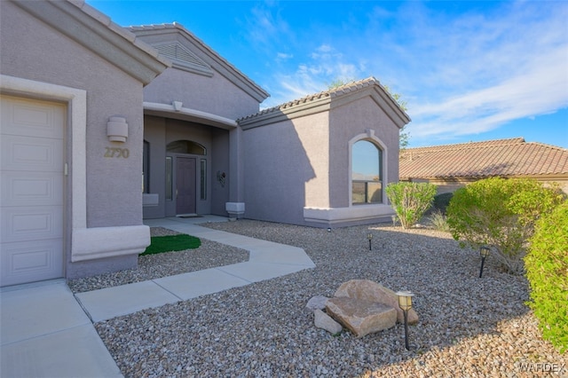 view of exterior entry with a garage, a tiled roof, and stucco siding