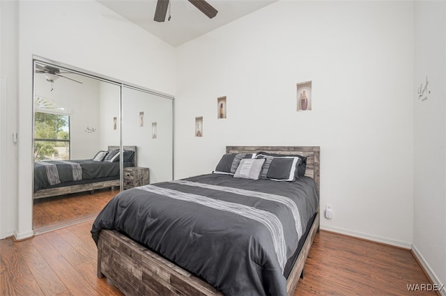 bedroom featuring a closet, a high ceiling, ceiling fan, wood finished floors, and baseboards