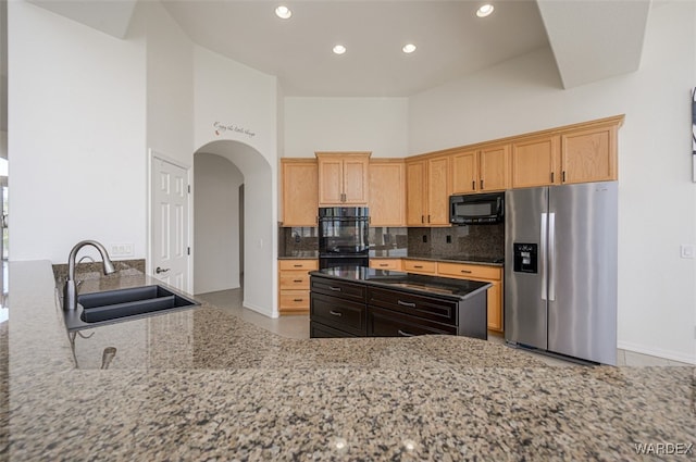 kitchen featuring arched walkways, light stone countertops, a sink, decorative backsplash, and black appliances