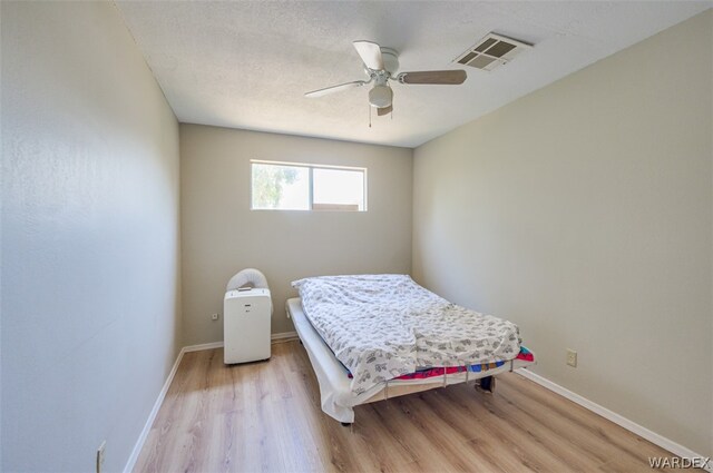 bedroom with ceiling fan, a textured ceiling, visible vents, baseboards, and light wood-style floors