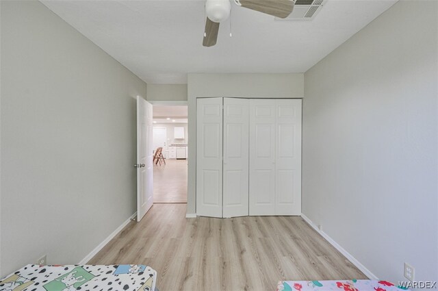 unfurnished bedroom featuring light wood finished floors, a ceiling fan, baseboards, and a closet