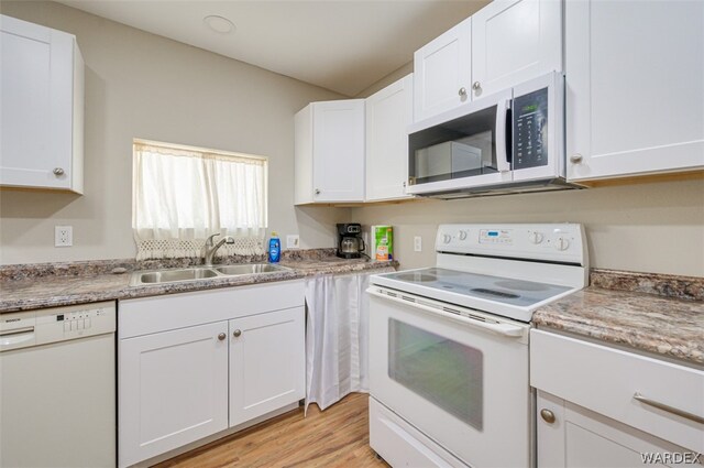 kitchen featuring light wood-type flooring, white appliances, white cabinets, and a sink