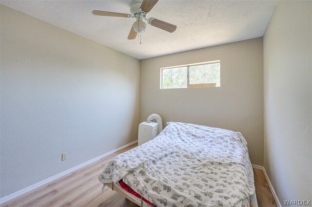 bedroom featuring light wood-style flooring, a textured ceiling, baseboards, and a ceiling fan