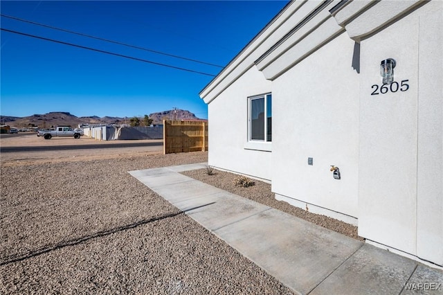 view of side of home featuring fence, a mountain view, and stucco siding