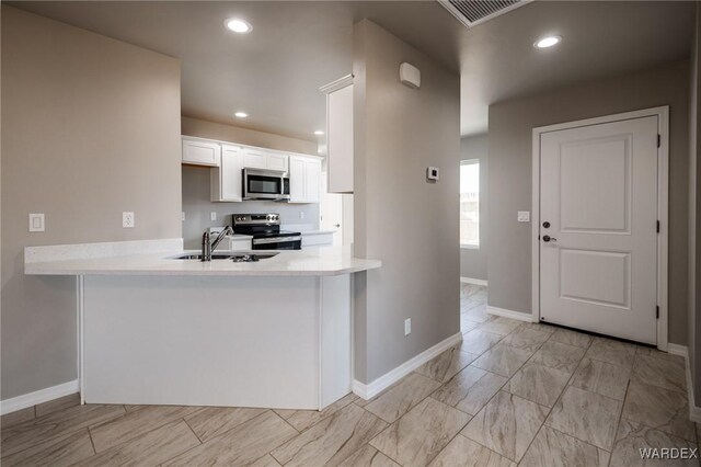 kitchen featuring stainless steel appliances, light countertops, a peninsula, and white cabinetry