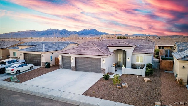 view of front of home with stone siding, an attached garage, a mountain view, and stucco siding