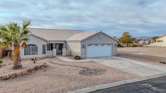 ranch-style house with driveway, a tile roof, an attached garage, and stucco siding