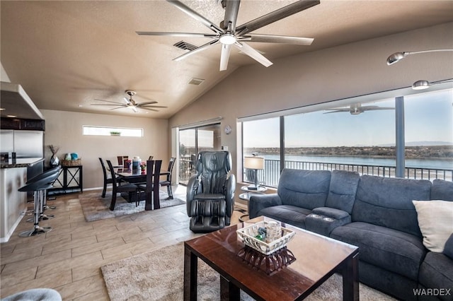 living room with visible vents, ceiling fan, a water view, vaulted ceiling, and a textured ceiling