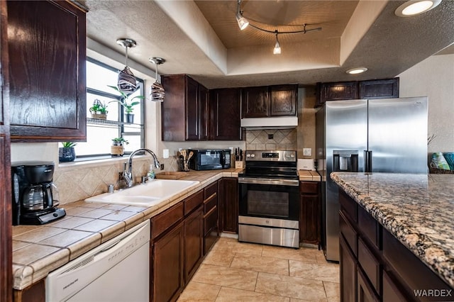 kitchen with stainless steel appliances, tile counters, a raised ceiling, a sink, and under cabinet range hood