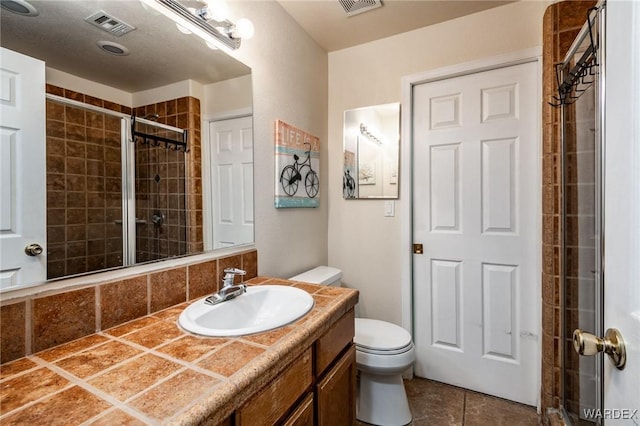 full bathroom featuring toilet, visible vents, tiled shower, and vanity