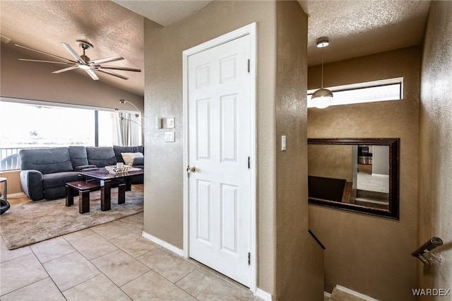 hall featuring a textured ceiling, a textured wall, lofted ceiling, light tile patterned flooring, and baseboards