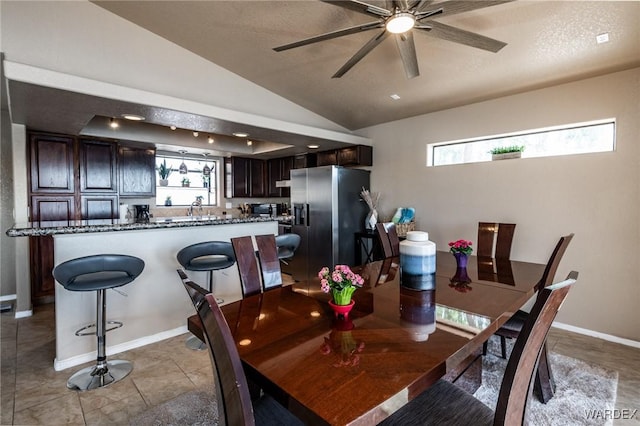 dining space featuring baseboards, a ceiling fan, vaulted ceiling, a textured ceiling, and light tile patterned flooring