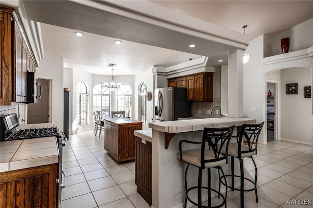 kitchen with a center island, tile countertops, hanging light fixtures, appliances with stainless steel finishes, and a peninsula