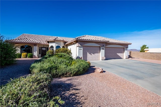 mediterranean / spanish-style house featuring an attached garage, a tile roof, concrete driveway, and stucco siding