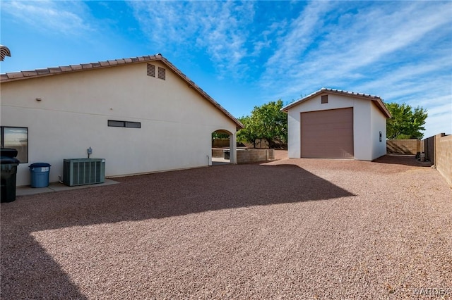 view of side of home featuring driveway, an outbuilding, fence, central air condition unit, and stucco siding