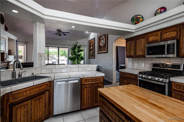 kitchen featuring arched walkways, stainless steel appliances, tasteful backsplash, a sink, and dark brown cabinets