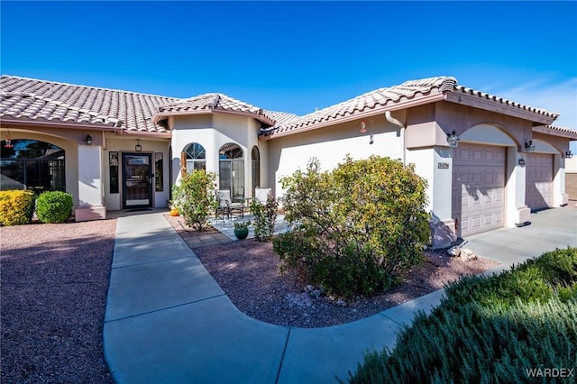 mediterranean / spanish-style house with a garage, a tiled roof, and stucco siding