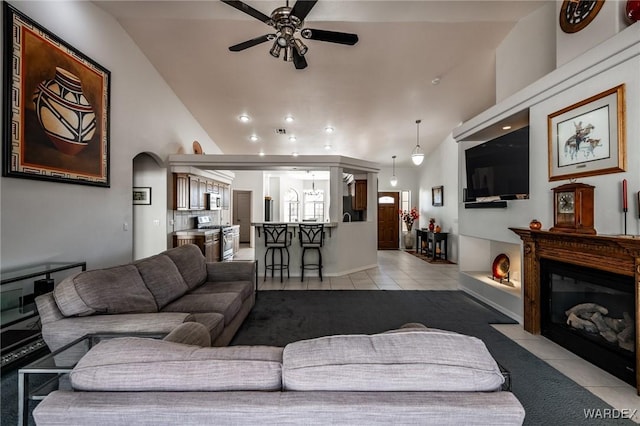 living area featuring a fireplace with flush hearth, vaulted ceiling, a ceiling fan, and light tile patterned flooring