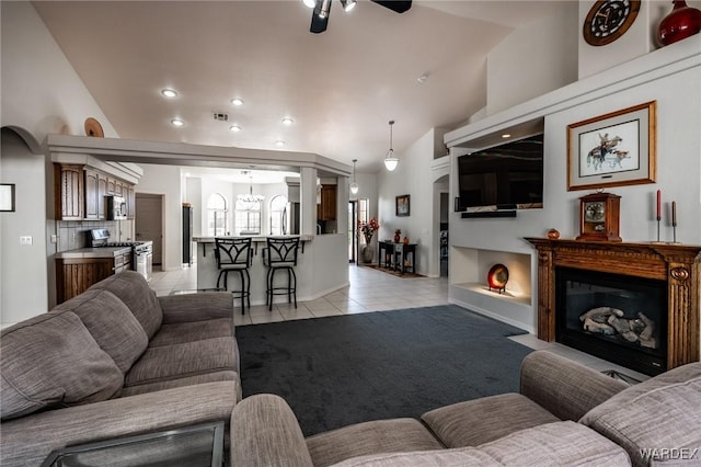 living area with light tile patterned floors, lofted ceiling, ceiling fan with notable chandelier, visible vents, and a glass covered fireplace