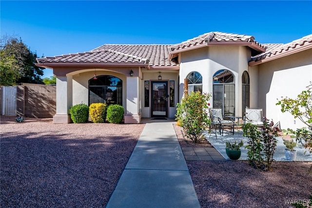 property entrance featuring a tiled roof, fence, and stucco siding