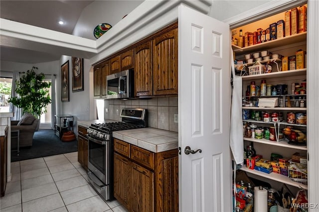 kitchen featuring light tile patterned flooring, dark brown cabinetry, stainless steel appliances, tile counters, and decorative backsplash