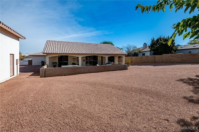 back of house featuring a fenced backyard, a tiled roof, and stucco siding