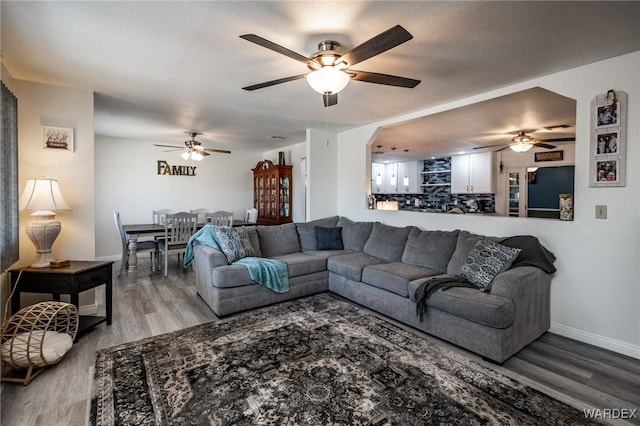 living area with arched walkways, wood finished floors, a ceiling fan, and baseboards