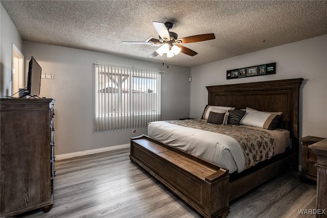 bedroom featuring ceiling fan, a textured ceiling, baseboards, and wood finished floors