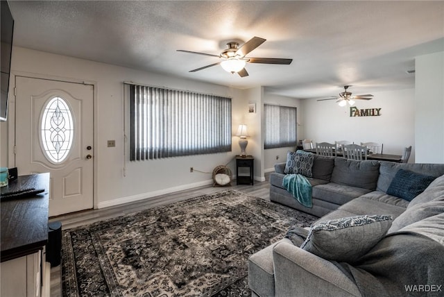 living room featuring ceiling fan, a textured ceiling, wood finished floors, and baseboards