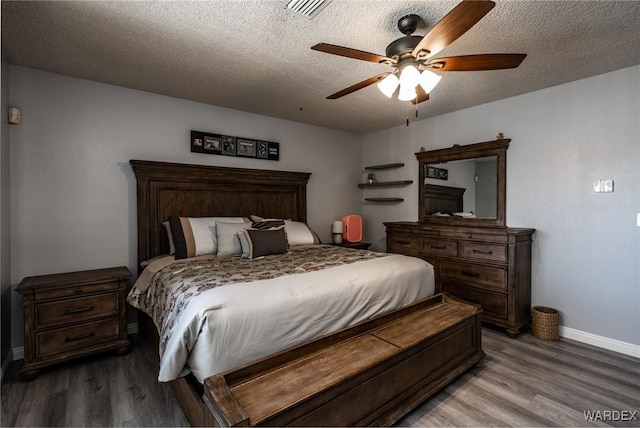 bedroom with visible vents, a textured ceiling, baseboards, and wood finished floors