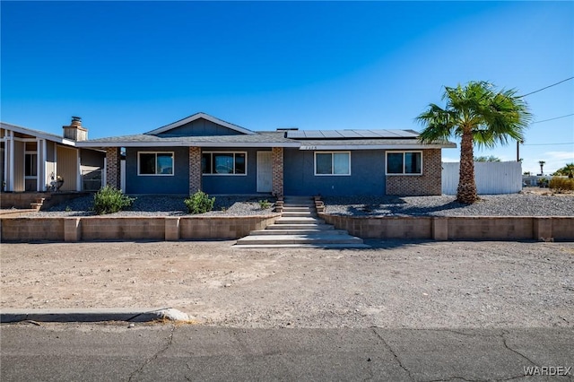 ranch-style home with roof mounted solar panels and brick siding