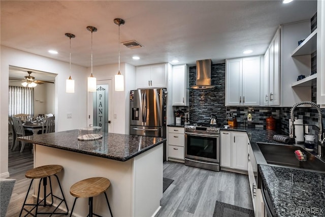 kitchen featuring visible vents, white cabinetry, a kitchen breakfast bar, appliances with stainless steel finishes, and wall chimney range hood