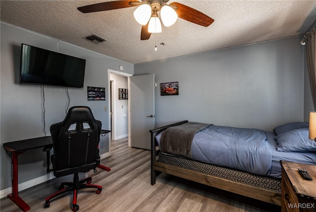 bedroom featuring a textured ceiling, a ceiling fan, baseboards, visible vents, and light wood-style floors