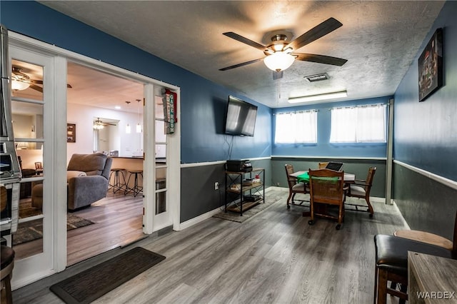 dining space with a textured ceiling, ceiling fan, wood finished floors, visible vents, and baseboards