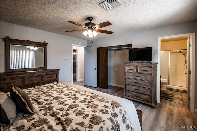 bedroom with a textured ceiling, wood finished floors, visible vents, a ceiling fan, and ensuite bath