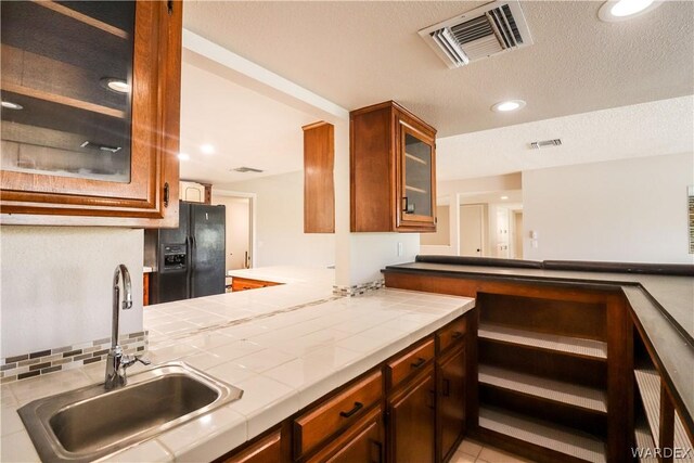 kitchen with tile countertops, visible vents, glass insert cabinets, a sink, and black fridge