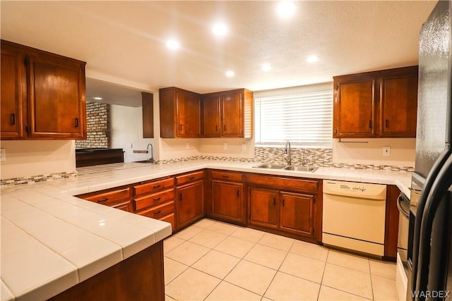 kitchen featuring tile counters, dishwasher, a peninsula, and a sink