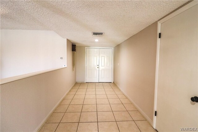 hall with light tile patterned floors, baseboards, visible vents, and a textured ceiling