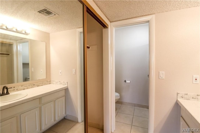 bathroom with a textured ceiling, tile patterned flooring, toilet, vanity, and visible vents