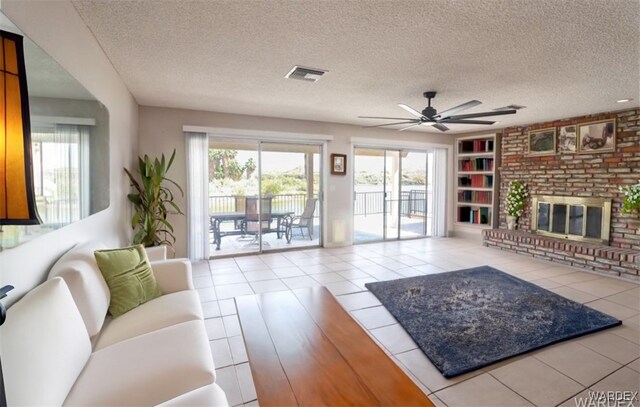 living room with a textured ceiling, light tile patterned flooring, a fireplace, visible vents, and built in features