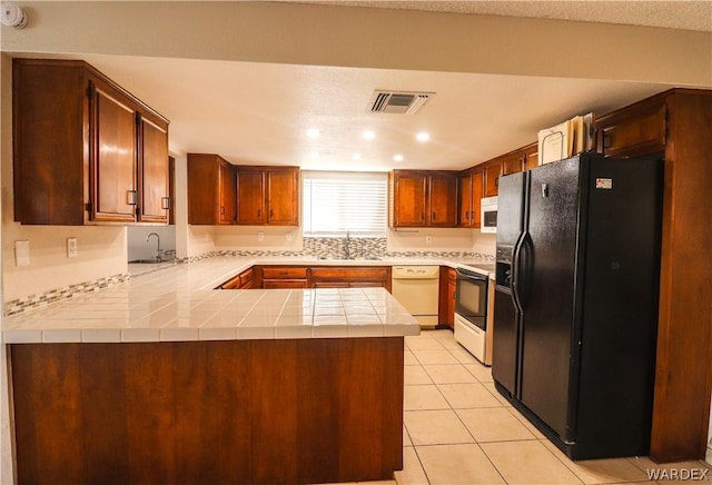 kitchen featuring light tile patterned floors, light countertops, a sink, white appliances, and a peninsula