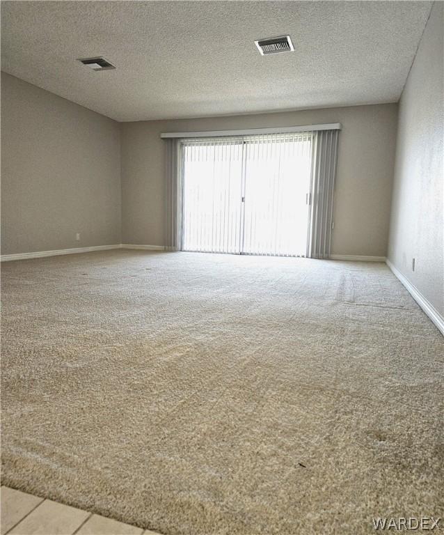 spare room featuring light carpet, a textured ceiling, visible vents, and baseboards