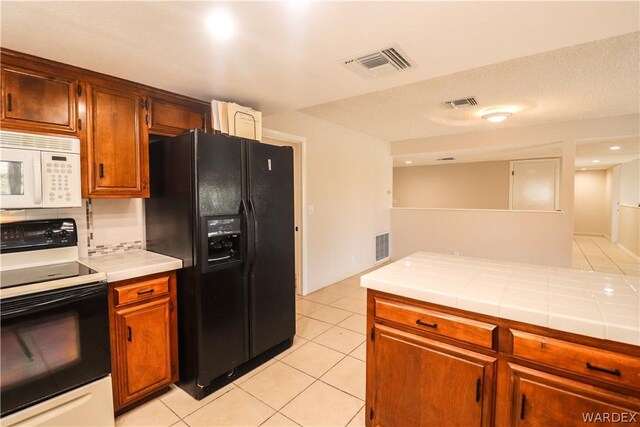 kitchen featuring visible vents, range with electric cooktop, tile counters, white microwave, and black refrigerator with ice dispenser