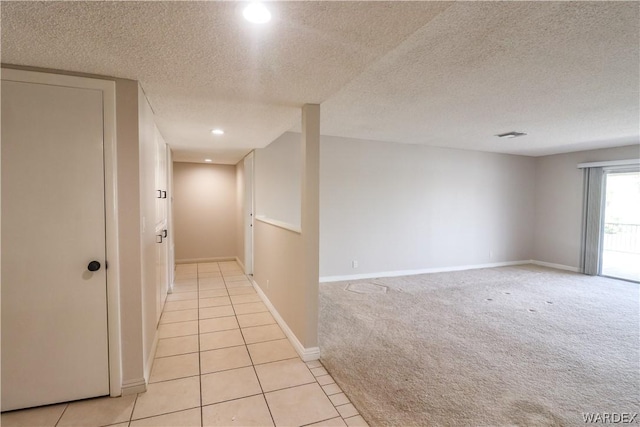 hall with baseboards, a textured ceiling, light tile patterned flooring, and light colored carpet