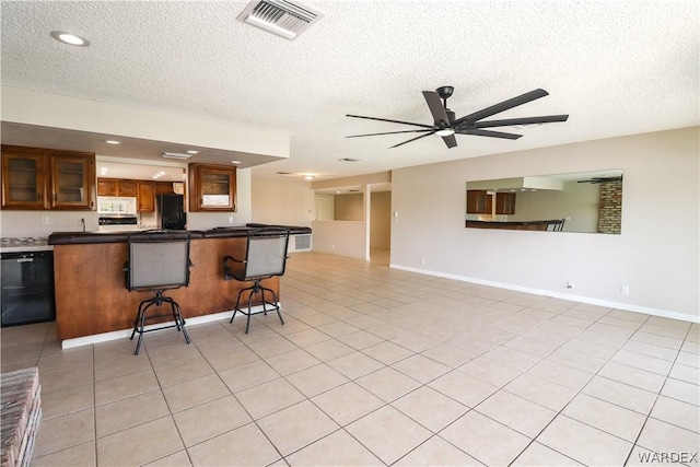 kitchen featuring a breakfast bar, visible vents, brown cabinets, black appliances, and glass insert cabinets