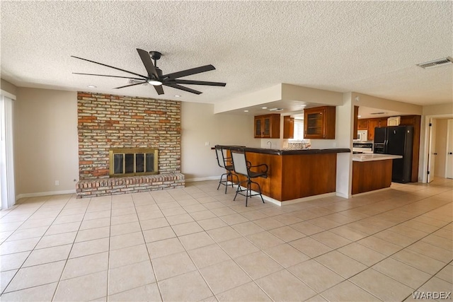 kitchen with a peninsula, open floor plan, a brick fireplace, brown cabinets, and black refrigerator with ice dispenser