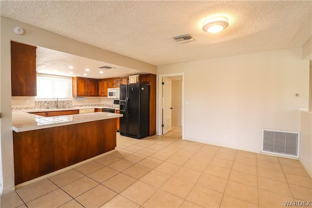 kitchen featuring visible vents, brown cabinetry, a peninsula, black refrigerator with ice dispenser, and light countertops